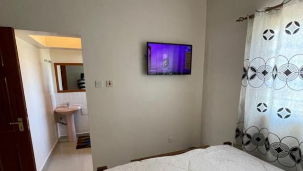 Un dormitorio con una cama, un televisor montado en la pared y un baño visible a través de una puerta abierta.