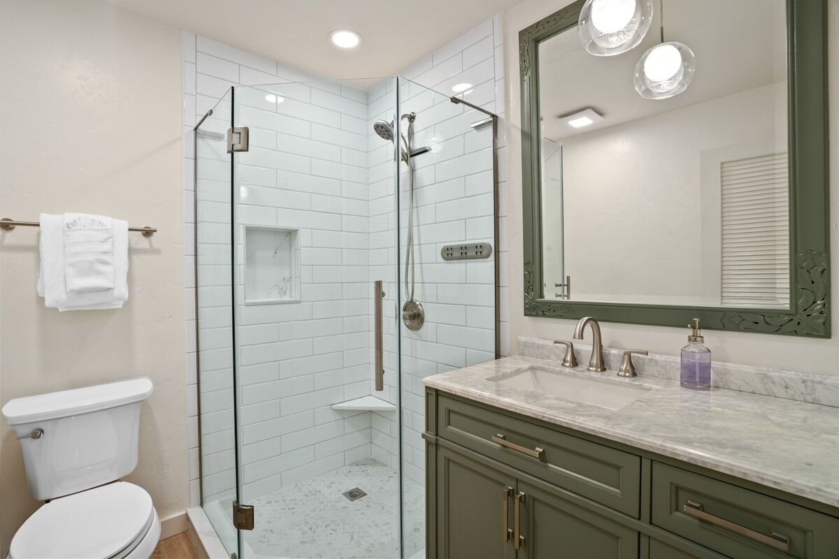 A modern bathroom with a glass-enclosed shower, white tiled walls, a white toilet, and a vanity with a marble countertop.