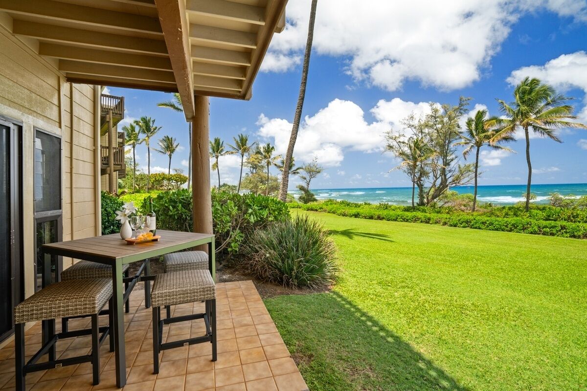 A patio with a table and chairs, a view of the ocean, and palm trees.