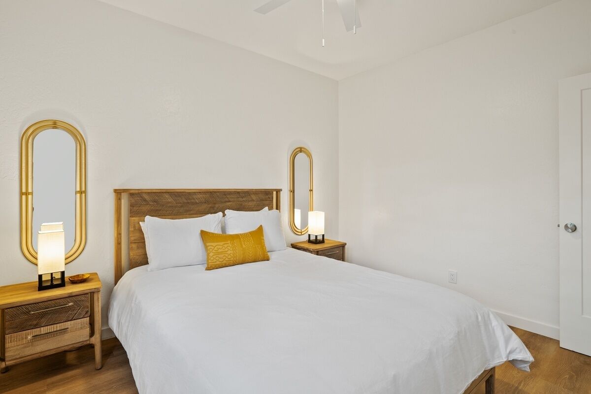 Een keurig opgemaakt slaapkamer met een groot bed, twee nachtkastjes met lampen, en twee spiegelwanden.