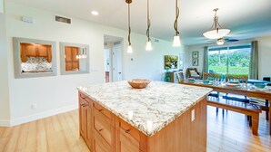 A spacious kitchen with a large island, wooden cabinets, and pendant lighting. - Kauai Pili Mai by Coldwell Banker Island Vacations (Koloa)