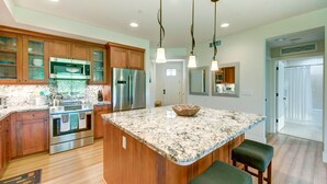 A modern kitchen with wooden cabinets, stainless steel appliances, a granite countertop, and pendant lighting. - Kauai Pili Mai by Coldwell Banker Island Vacations (Koloa)