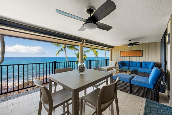 A balcony with a dining table, chairs, and a sofa with blue cushions.