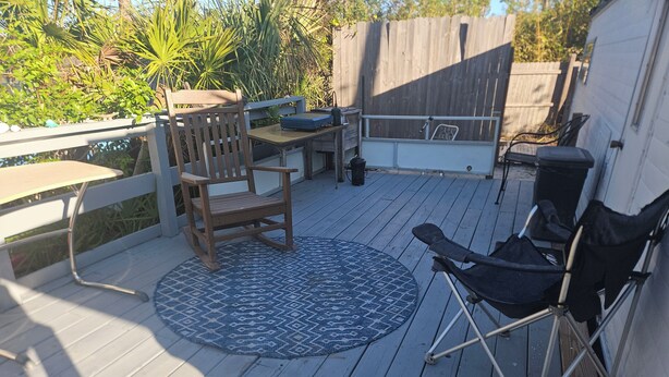 Une terrasse avec une chaise en bois, un tapis bleu à motifs et une chaise pliante noire.