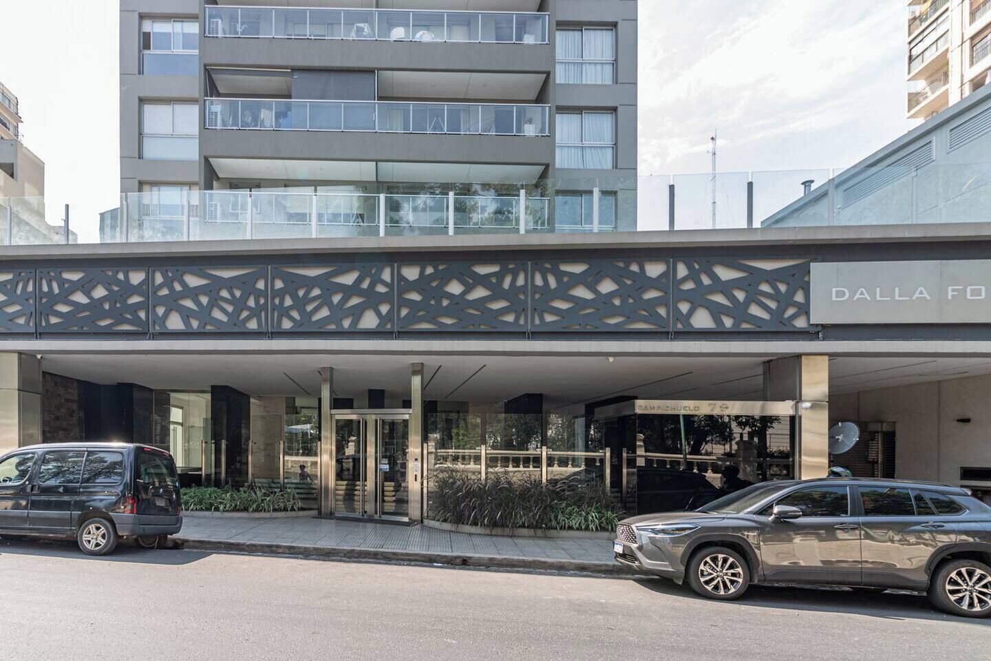 Un bâtiment moderne doté d’une entrée couverte, avec deux voitures garées devant, et une enseigne indiquant « DALLA FORUM ».