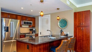 A modern kitchen with a large island, stainless steel appliances, wooden cabinets, and a decorative backsplash. - Honua Kai Hokulani by Coldwell Banker Island Vacations (Lahaina)