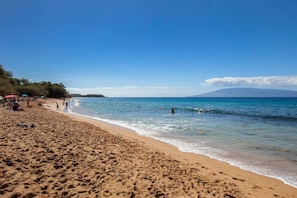 A beach with clear blue water, people swimming, and a mountain in the background. - Honua Kai Hokulani 310 2 Bedroom Condo (Lahaina)