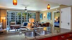 A modern kitchen with a double sink, pendant lighting, and a view of the outside balcony. - Honua Kai Hokulani by Coldwell Banker Island Vacations (Lahaina)