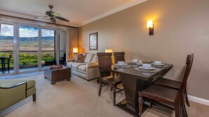 A hotel room with a dining area, a sofa, a table set for four, and a view of the outdoors. - Honua Kai Hokulani by Coldwell Banker Island Vacations (Lahaina)