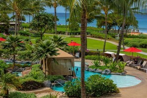 A resort pool area with palm trees, a beach view, and red umbrellas.