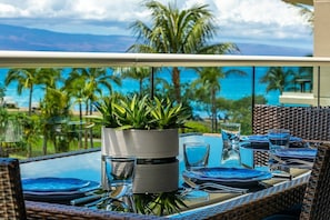 A dining table set for two with a view of the ocean and palm trees. - Honua Kai Hokulani 310 2 Bedroom Condo (Lahaina)