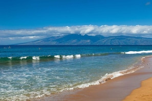 A beach with clear water, a sandy shore, and a mountain range in the background. - Honua Kai Hokulani 310 2 Bedroom Condo (Lahaina)