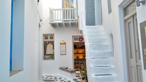 A narrow, white-walled alley with stone steps and a small staircase leading to a balcony.