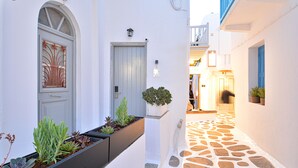 A narrow stone-paved alleyway with white walls and blue doors, leading to a building with a balcony.