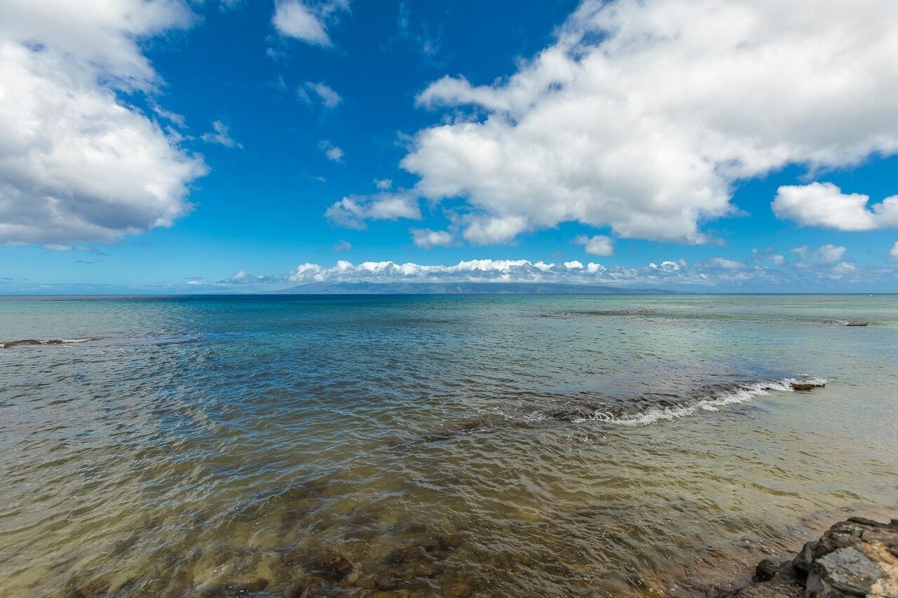Een strand met helder ondiep water, verre bergen en een gedeeltelijk bewolkte lucht.