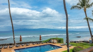 A swimming pool with lounge chairs and umbrellas, overlooking a beach with palm trees and ocean waves. - Hale Kai by Coldwell Banker Island Vacations (Lahaina)