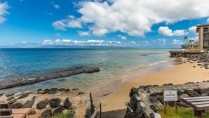A beach with a caution sign, rocky shoreline, and a building with a balcony. - Hale Kai by Coldwell Banker Island Vacations (Lahaina)