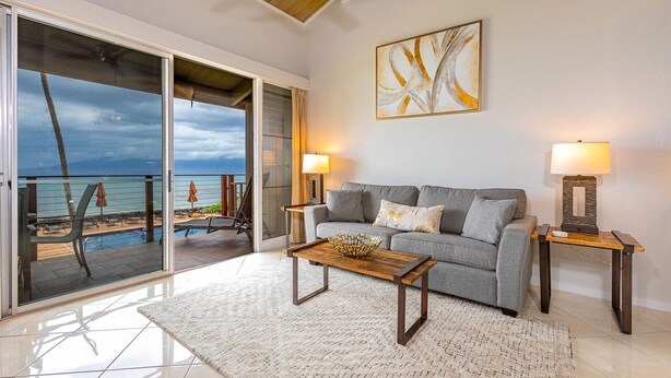 A living room with a grey sofa, two side tables with lamps, a wooden coffee table, and a large abstract painting on the wall. - Hale Kai by Coldwell Banker Island Vacations (Lahaina)