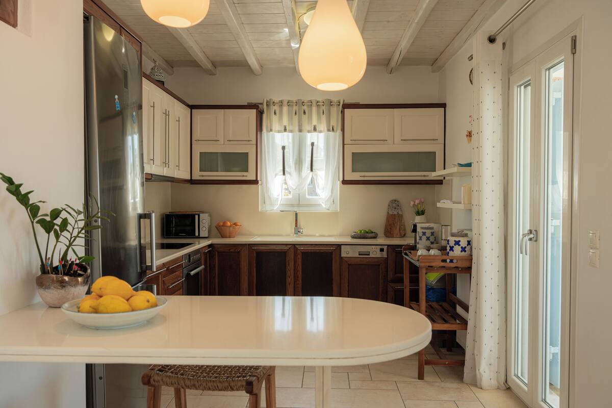 A kitchen with a central island, wooden cabinets, a stainless steel refrigerator, and pendant lighting.