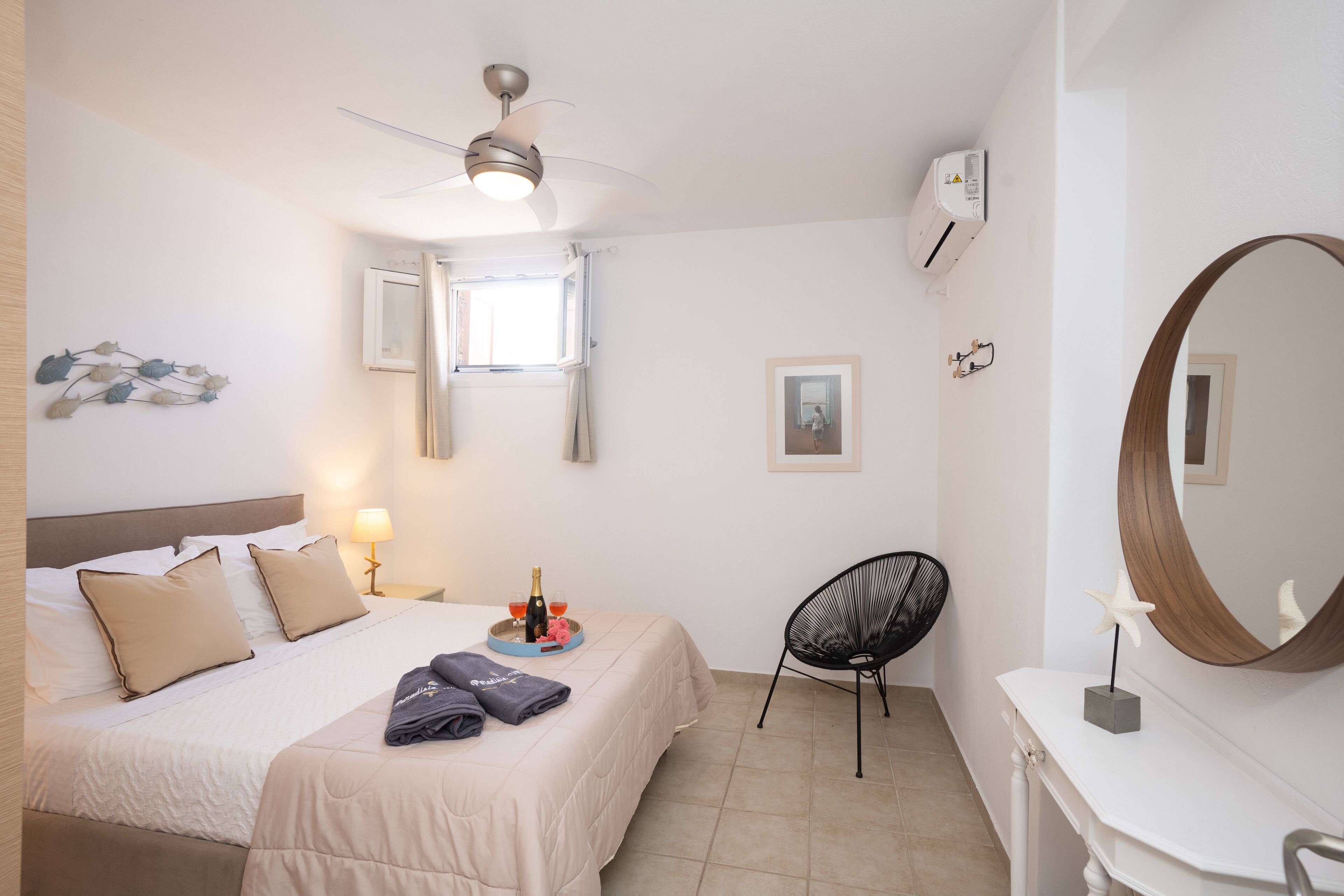 A hotel room with a bed, a chair, a vanity, a ceiling fan, and a window.