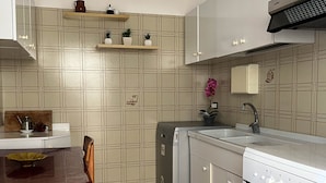 Een keuken met een eettafel, stoelen, een koelkast, een vaatwasser, een fornuis en een spoelbak.
