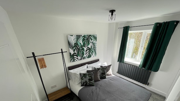 Une chambre à coucher avec un lit, un radiateur, une fenêtre avec des rideaux et un luminaire fixé au mur.