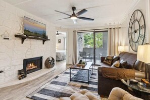 Un salon doté d’une cheminée, d’un ventilateur de plafond, d’une grande horloge et offrant une vue à travers une porte vitrée.