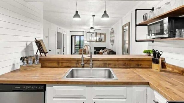 Een moderne keuken met een houten aanrechtblad, witte kasten, een roestvrijstalen spoelbak en hangende lampen.