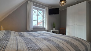 A bedroom with a large bed, a window with curtains, a TV mounted on the wall, and a wardrobe. - Doppelhaushälfte für 6 Personen mit Wlan (Graal-Müritz)