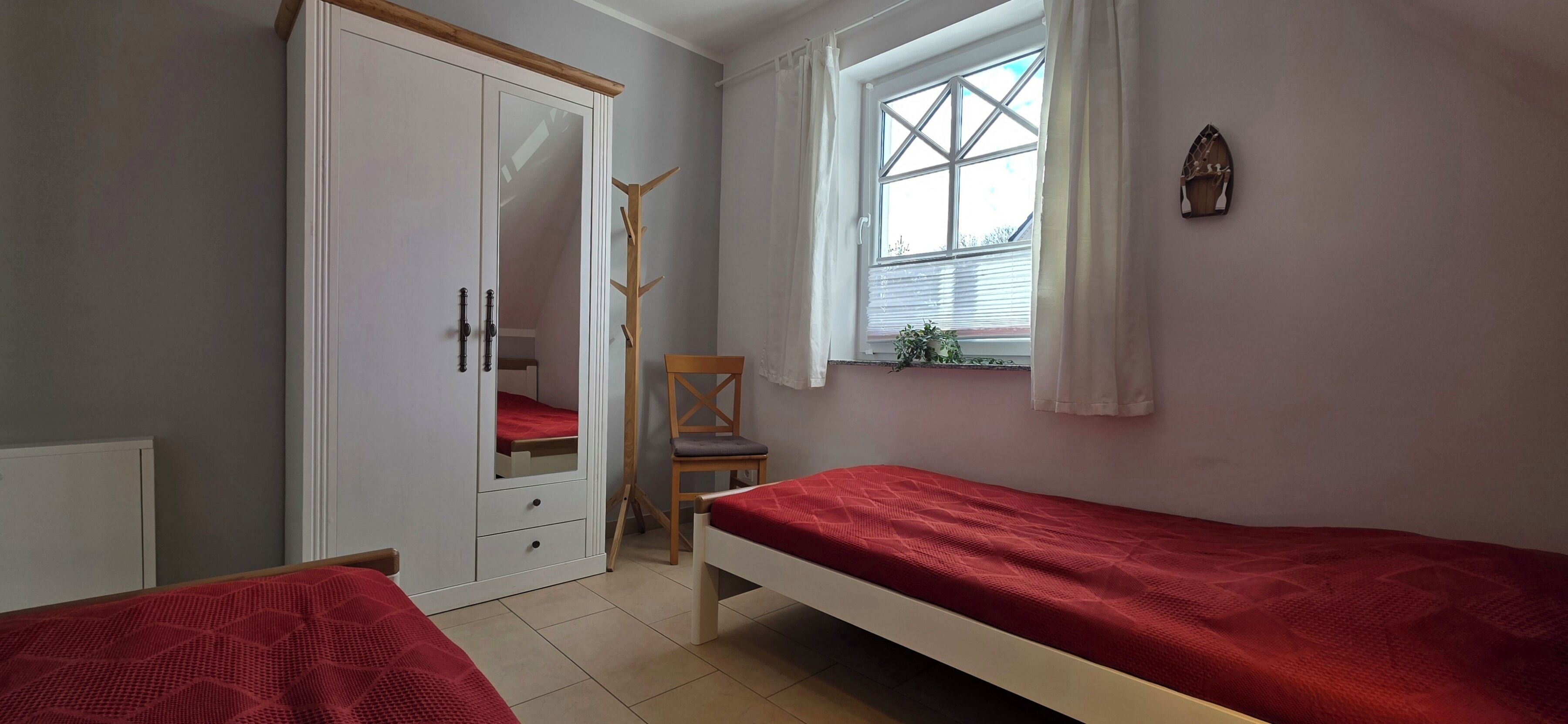 Una camera da letto con due letti singoli, un armadio, una sedia e una finestra con tende.
