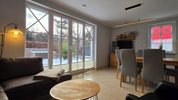 A modern living room with a sofa, a round table, and a dining area with chairs and a wooden table. - Doppelhaushälfte für 6 Personen mit Wlan (Graal-Müritz)
