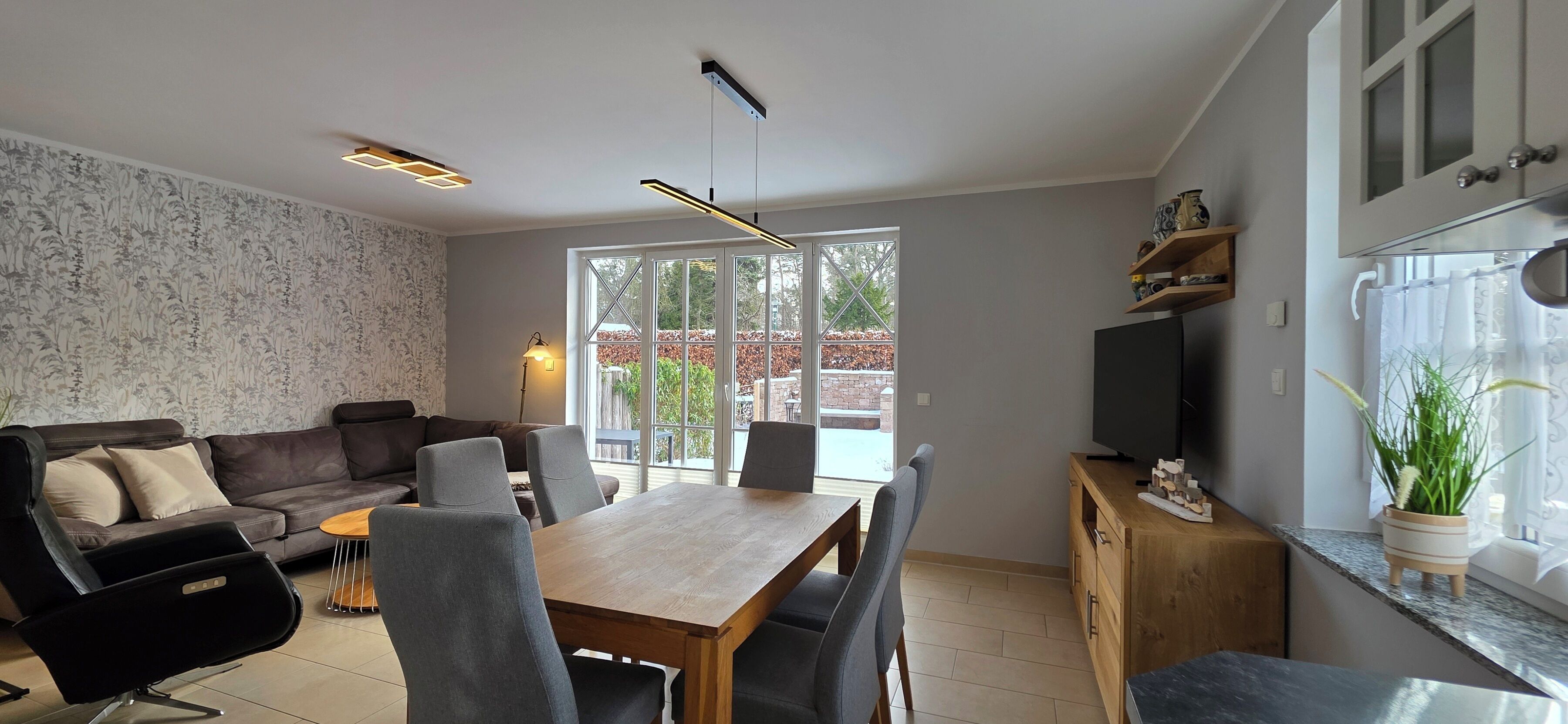En moderne stue med sofa, spisebord, stole og et fjernsyn på et træskab.