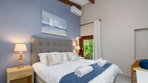 A neatly made bed with a blue blanket, a bedside lamp, and a painting of a sailboat on the wall. - San Lameer Villa 3204 (Southbroom)