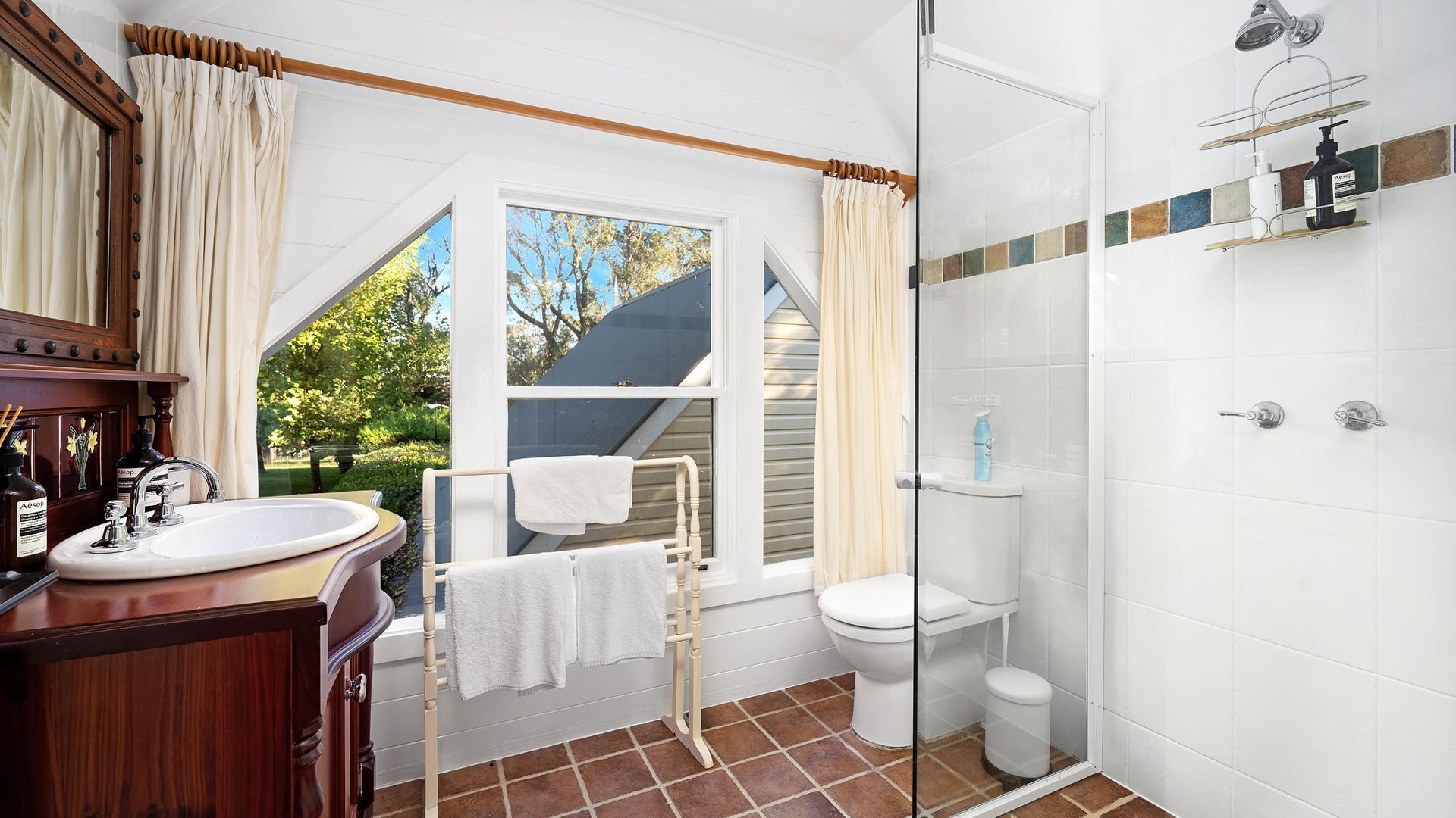 A bathroom with a wooden vanity, a glass shower enclosure, and a window providing a view of the outdoors.