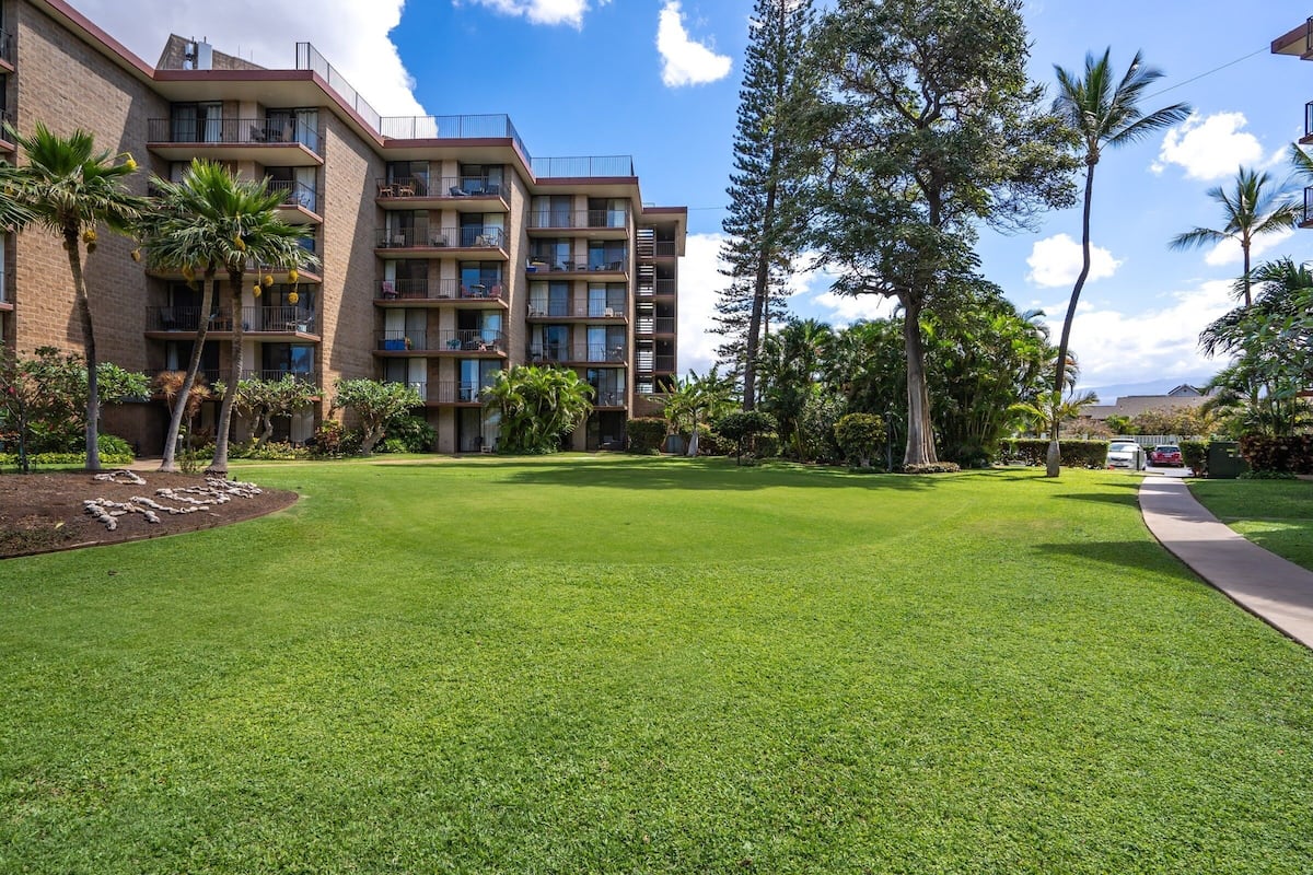 A hotel courtyard with a well-maintained lawn, palm trees, and a multi-story building with balconies.