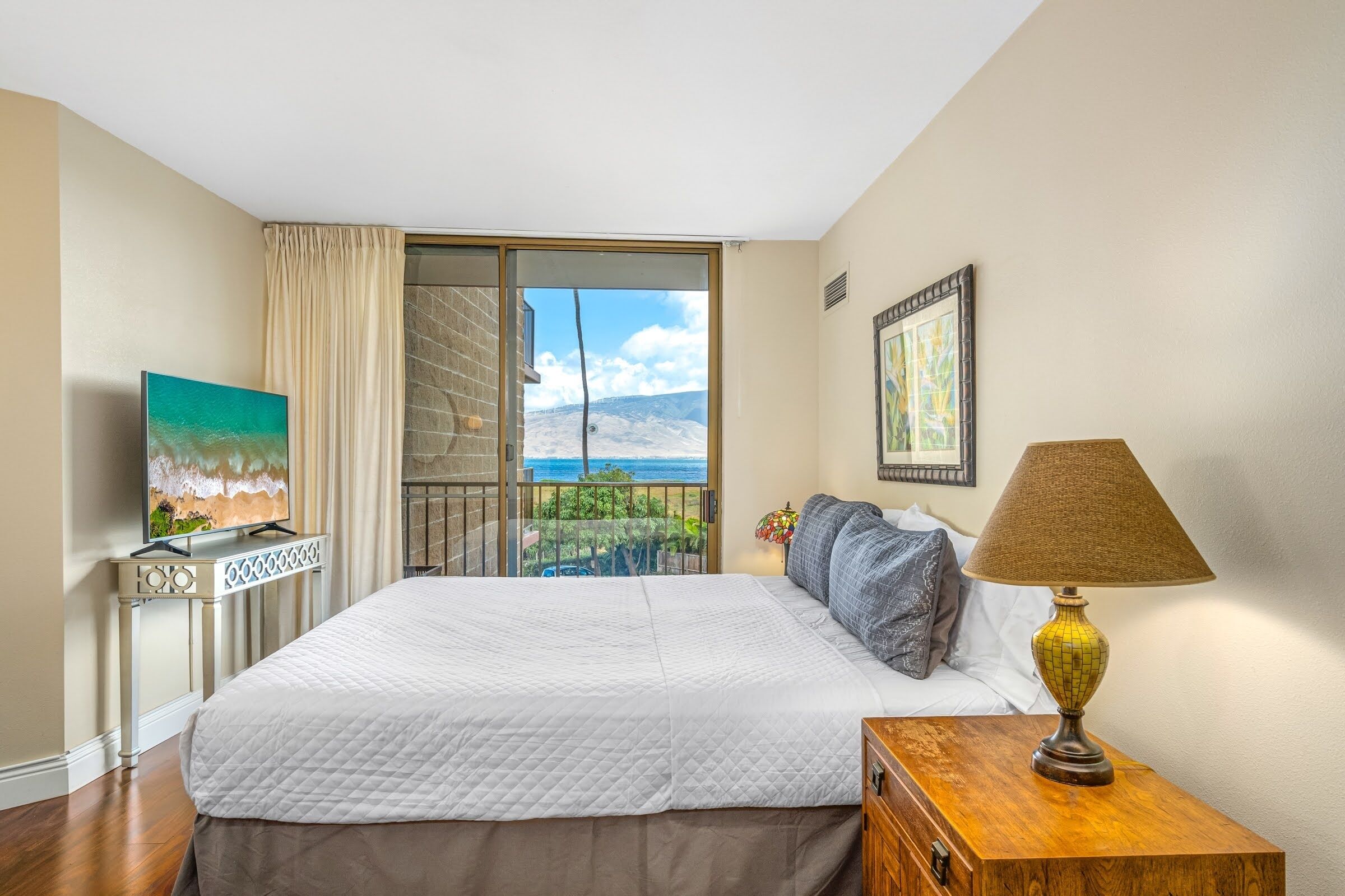 A bedroom with a large bed, a TV, a lamp, and a view of the sea.