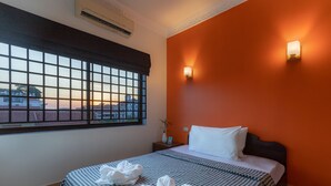 A hotel room with a large window, a bed with checkered bedding, and a wall-mounted light fixture.