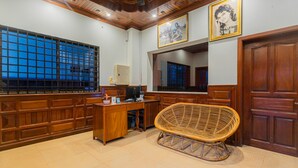 A room with a wooden desk, a wicker chair, a large window with a grid pattern, and a door with a mirror above it.