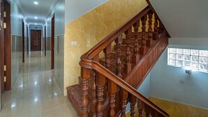A spacious hallway with a polished marble floor, a wooden staircase with ornate balusters, and a large window with a grid pattern.