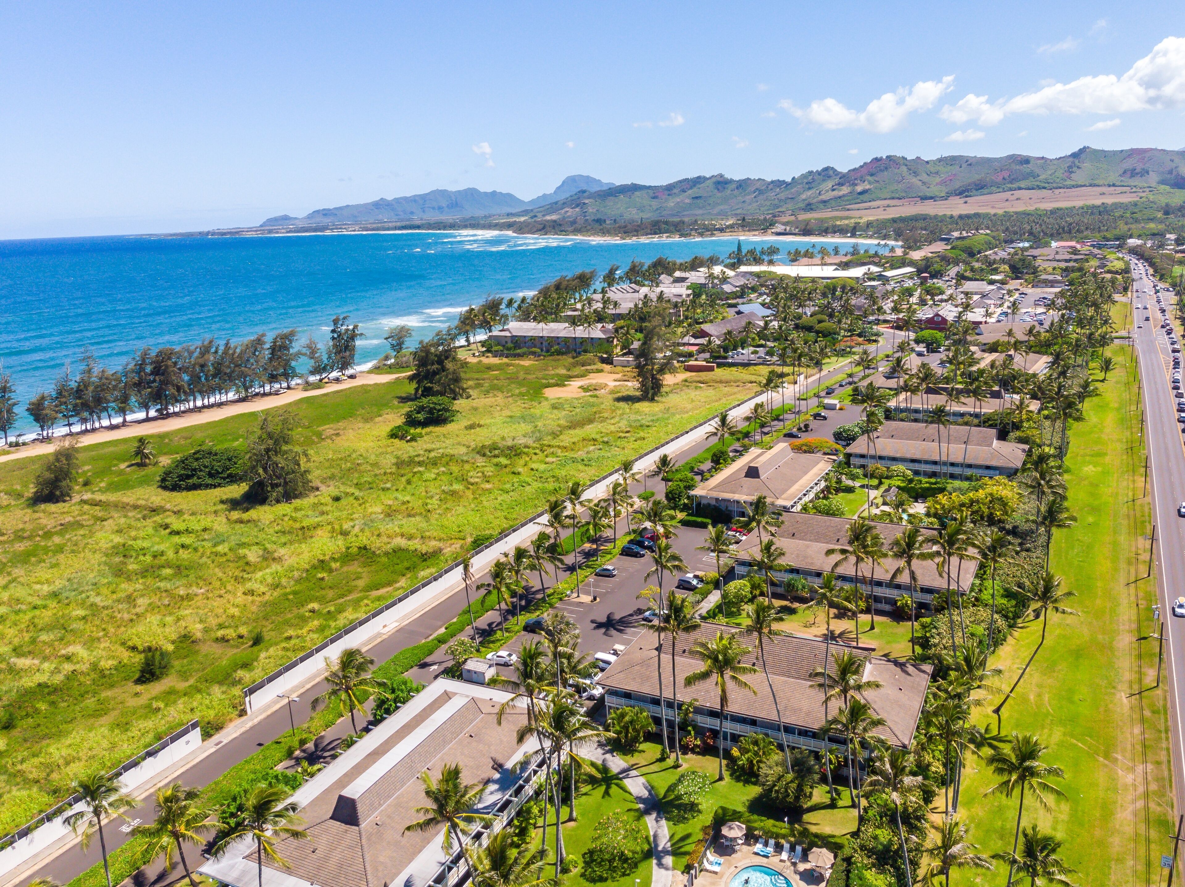 An aerial view of a coastal residential area with a beachfront, roads, and buildings.
