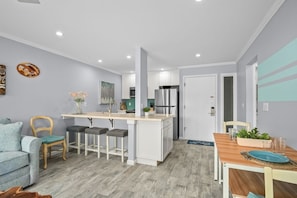 Une cuisine moderne avec des meubles blancs, un îlot central et un coin repas comprenant une table et des chaises en bois.