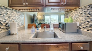 A kitchen with a granite countertop, stainless steel sink, wooden cabinets, and a microwave. - Kauai Plantation Hale Suites by Coldwell Banker Island Vacations (Kapaa)