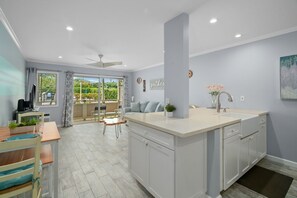 Uma cozinha moderna com uma ilha central, área de jantar com mesa e cadeiras, e vista para o exterior através de grandes janelas.