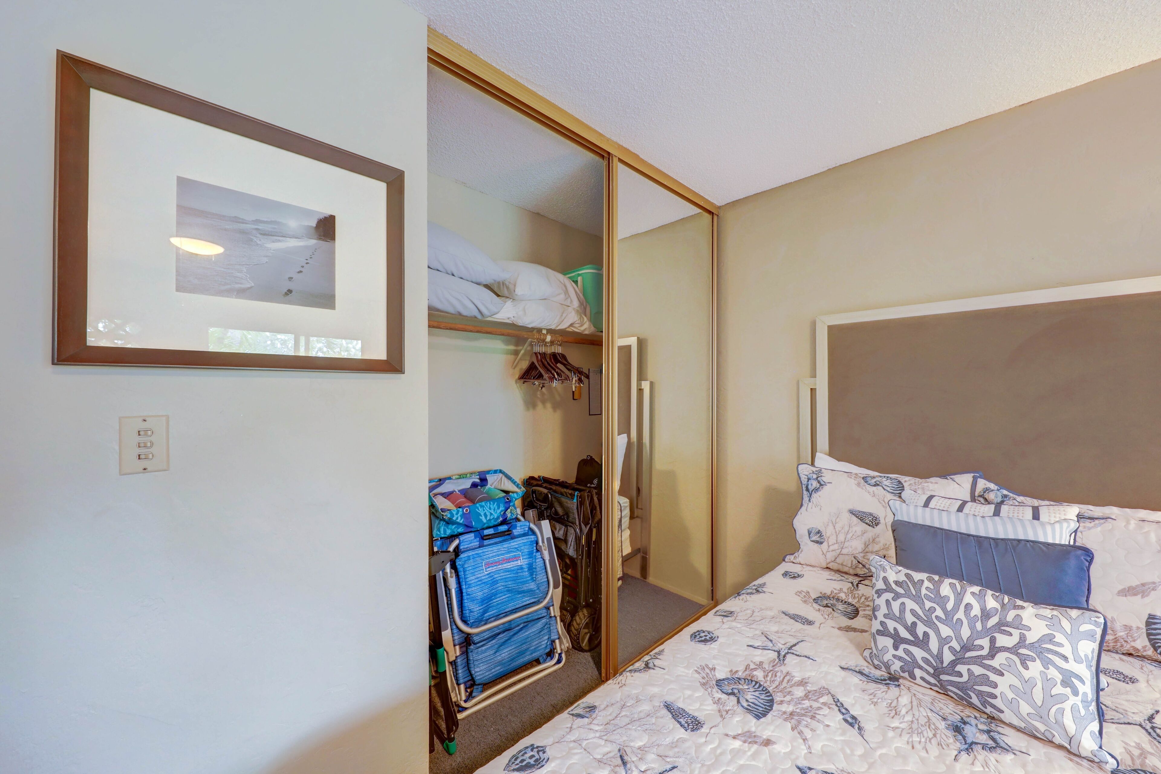 A bedroom with a bed, a closet with hanging clothes, and a framed picture on the wall.