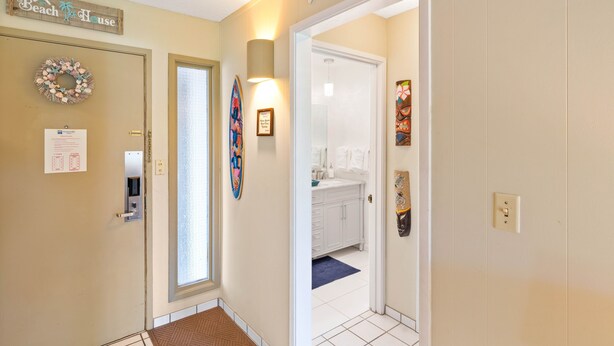 Un couloir avec une enseigne en bois indiquant « Beach House », une porte dotée d’un panneau en verre dépoli, et une salle de bain visible à travers la porte.