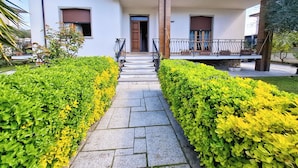 A modern house with a paved pathway leading to the entrance, surrounded by well-maintained hedges.