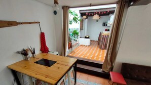Un coin repas avec une table et des chaises en bois, un petit banc et une vue sur un espace cuisine doté d’un sol carrelé et d’une table à manger.