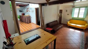 Un salon avec un canapé marron, un canapé jaune, une table en bois et un coin cuisine visible à travers une porte ouverte.