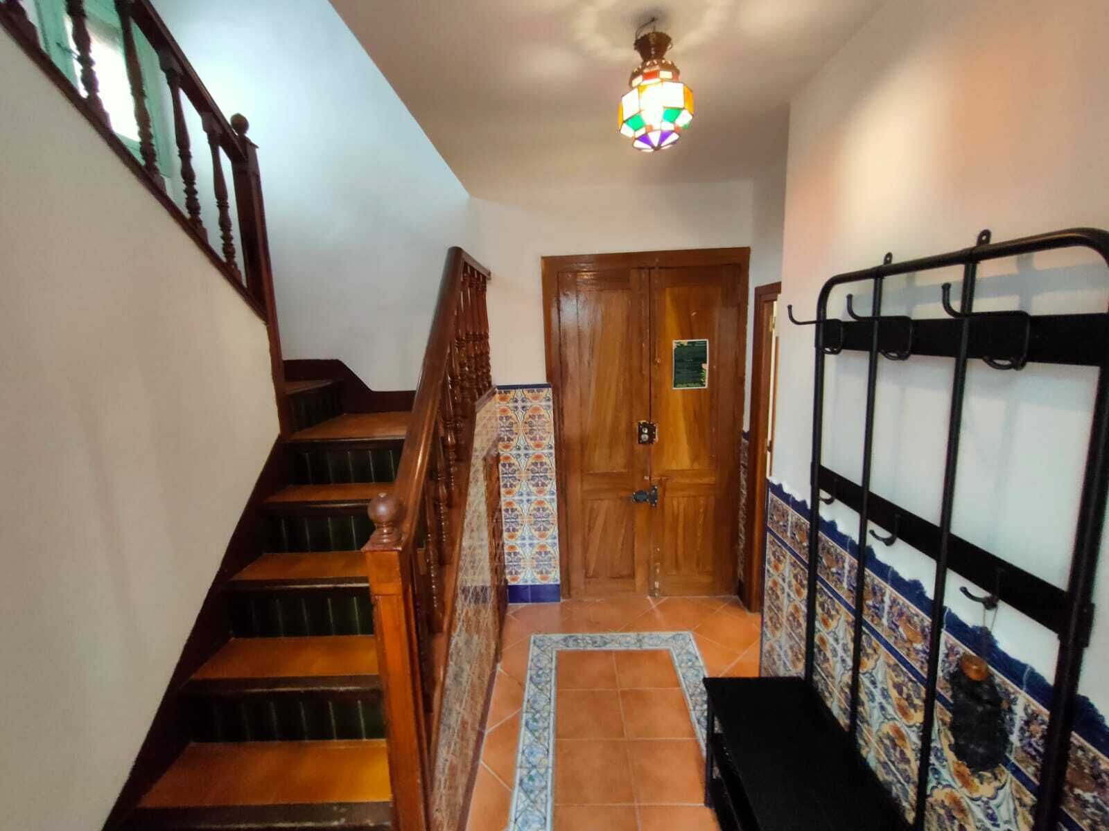 Un escalier avec des marches en bois et une rampe, menant à une porte ornée d’une bordure de carreaux colorés.