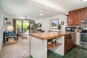 Una cocina moderna con armarios de madera, microondas integrado y estufa. Hay una zona de comedor con mesa y sillas, y un ventanal con vistas a zonas verdes.